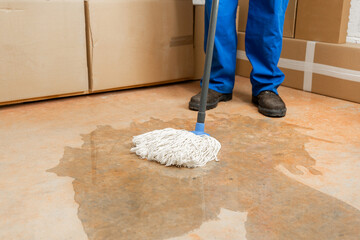 Male worker cleaning-up a slip hazard on the floor of an industrial plant with white mop.