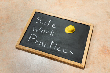 Small chalkboard with the text Safe Work Practices and yellow hard hat. Concepts of safety, precaution, and standards in the workplace.Blackboard on a cement background
