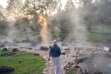 Obraz premium Woman Walking Along Stone Path at Steaming Natural Hot Springs in Thailand.