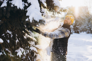 Man enjoying snow falling from evergreen tree, playing outdoors during winter day with sunlight