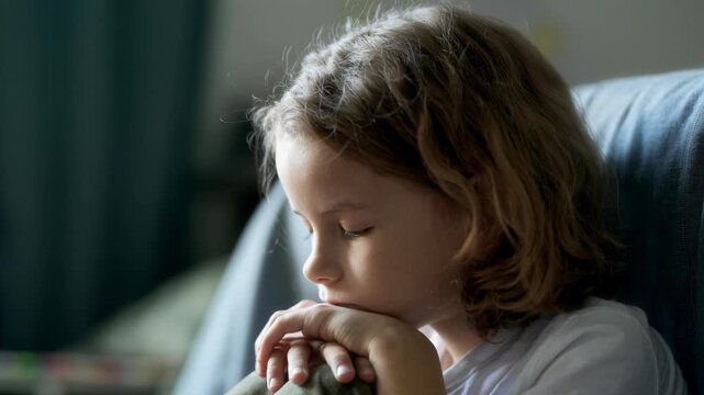 Close up of sad boy child sitting on floor near bed with eyes closed and breathing slowly to calm down, AI generated footage