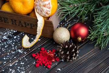 Orange mandarins in wooden box with fir apple, red balls, snowflakes on green fir branch background
