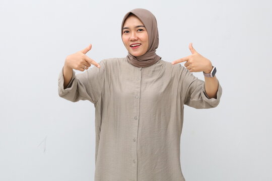 Cheerful, enthusiastic, cheerful young Asian woman in hijab pointing at herself with index finger, isolated on white background.