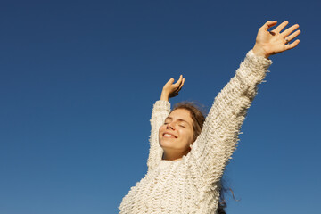 freedom-loving, happy young European woman in her twenties enjoys moment standing in sun under a cloudless sky. I love life, well-being, positive thinking, and dreaming. Walking in spring outdoors © Anna