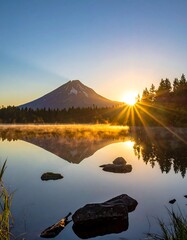 A serene morning scene featuring a snow-capped peak mirrored in calm water, with a bright sunburst illuminating the landscape