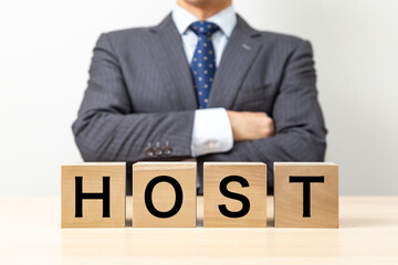Obraz premium 「HOST 」と書かれたブロックと腕組みをするビジネスマン