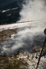 Fototapeta premium Forest fire. Fire burns grass and land near mountains with smoke rising into the air in a forest fire situation. Hiking in Carpathian Mountains, Ukraine