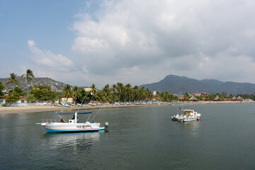 Obraz premium View of the beach in the bay of Ixtapa Zihuatanejo with boats in the sea and palm trees on the sand. Tropical landscape of costa grande, Guerrero. Mexico, January 19, 2026.