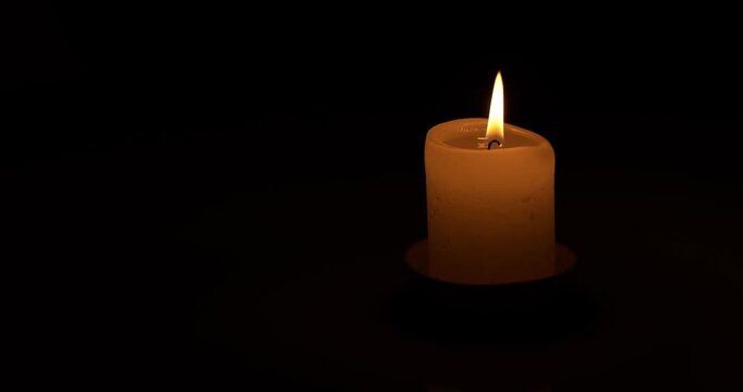 Candle burns on a dark background. Candle flame moves in the wind.