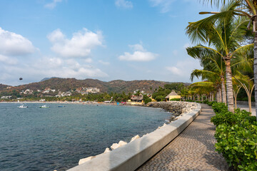 Fototapeta premium El Capricho del Rey Boardwalk at La Ropa Beach, Ixtapa Zihuatanejo, Guerrero. Coastal walkway decorated with coconut palms and nature facing the sea. Mexico.