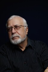 Obraz premium Older man with glasses looking thoughtfully to the side against a dark background in a simple indoor setting