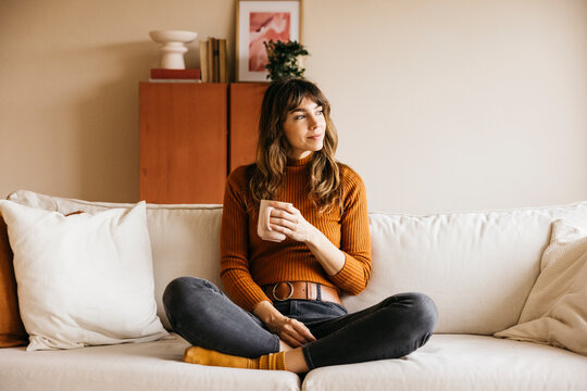 Woman enjoying a cozy moment of relaxation, holding a mug and looking away while thinking