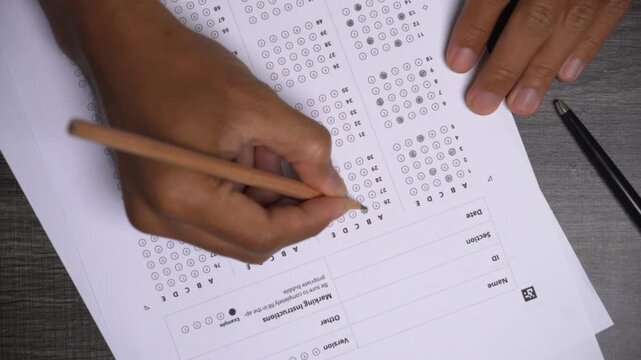 Person filling in optical mark reader answer sheet bubbles with a pencil during an academic examination