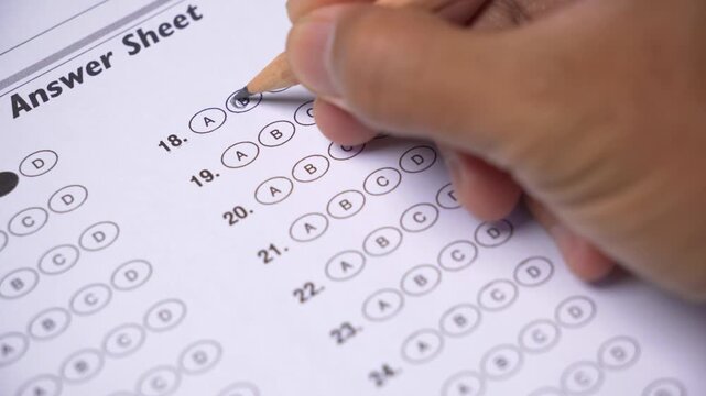 Hand shading multiple choice answer sheet circles with a pencil during an examination or test