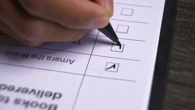 Close up view of a person's hand with a pen marking or ticking multiple checkboxes on a document or survey form
