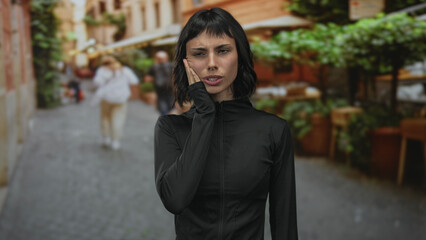 Woman in black casual jacket holds cheek with hand on busy urban street for toothache  discomfort. © Krakenimages.com