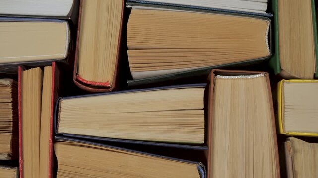 Stacked hardcover books viewed from above forming textured paper pattern, Closeup composition showing varied page edges bindings and covers in storage