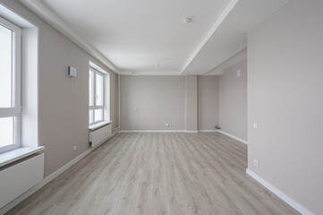 Obraz premium bright, empty room with light grey walls, wooden-style laminate flooring, two large windows, white baseboards, recessed ceiling, and built-in radiators. Minimalist, ready for furnishing.