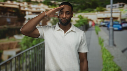 Man saluting with hand to forehead on street near railing and lamppost, wearing white polo shirt...