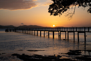 Obraz premium Silhouette of wooden pier stretching into the calm sea at golden sunset