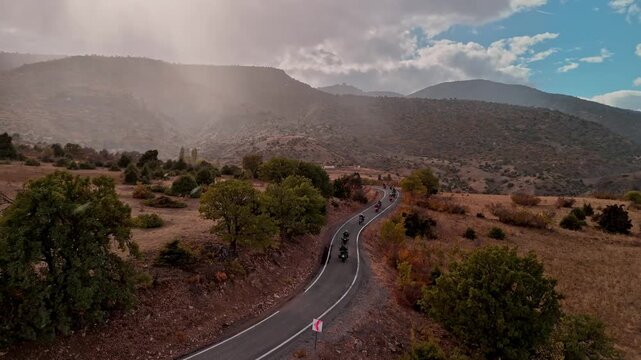 Aerial view of a motorcycle convoy riding on a winding road in Erzincan, Turkey, surrounded by natural terrain and curves, ideal for travel, adventure and cinematic road trip concepts.