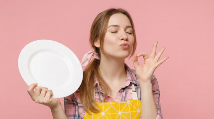 A happy woman wearing an apron shows food satisfaction with an empty plate and an okay gesture.
