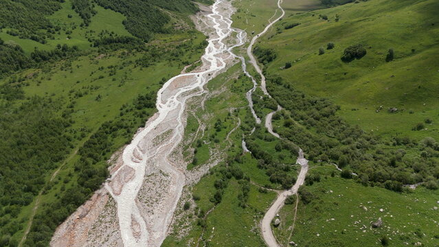 Aerial drone view of a lush mountain valley near Ushguli, one of the highest continuously inhabited villages in Europe, located in the Svaneti region of Georgia. A winding river flows through green al