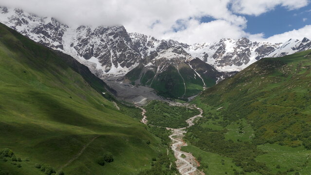 Aerial drone view of a lush mountain valley near Ushguli, one of the highest continuously inhabited villages in Europe, located in the Svaneti region of Georgia. A winding river flows through green al