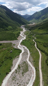 Aerial drone view of a lush mountain valley near Ushguli, one of the highest continuously inhabited villages in Europe, located in the Svaneti region of Georgia. A winding river flows through green al