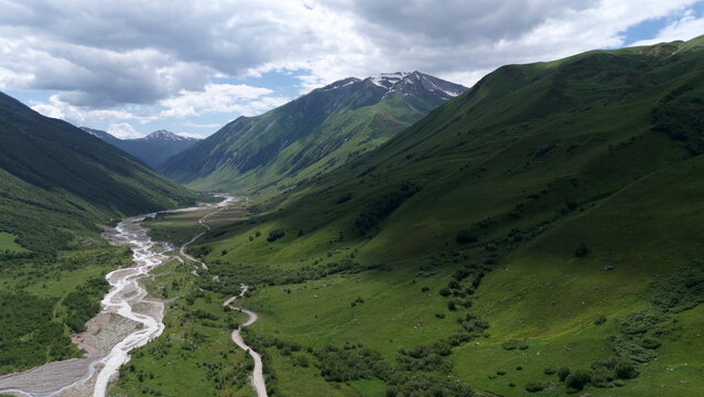Aerial drone view of a lush mountain valley near Ushguli, one of the highest continuously inhabited villages in Europe, located in the Svaneti region of Georgia. A winding river flows through green al