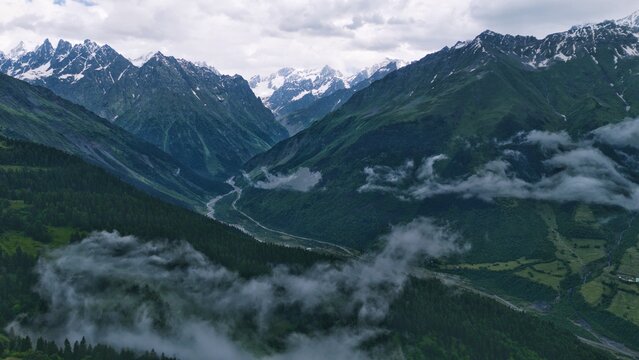 Aerial drone landscape of Mount Ushba, one of the most iconic peaks of the Caucasus Mountains, overlooking the green valleys and alpine villages near Mestia in the Svaneti region of Georgia. Snow-capp