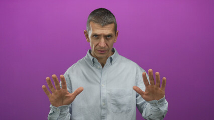 Naklejka premium Caucasian man in striped shirt makes calm gesture against vibrant pink background, exuding a sense of tranquility through expressive hand movements and focused demeanor.