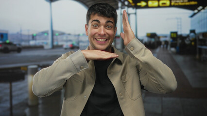 Man shows hands framing camera in airport lounge while guy lifts palm gesture near terminal desk...