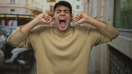 Man presses ears to cover blaring street horns as hispanic male stands outdoor amid noise with rising annoyance and discomfort. © Krakenimages.com