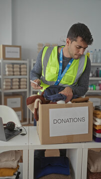 Man places clothes into a box while sorting at a warehouse with a hispanic young volunteer collecting donations for a male charity group.