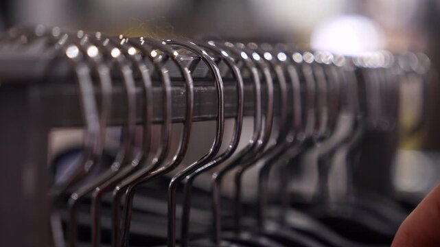 Clothing hanger selection macro video of a hand taking a garment from metal clothes hangers on a rack. Shallow depth of field, retail shopping concept, fashion and consumer choice.