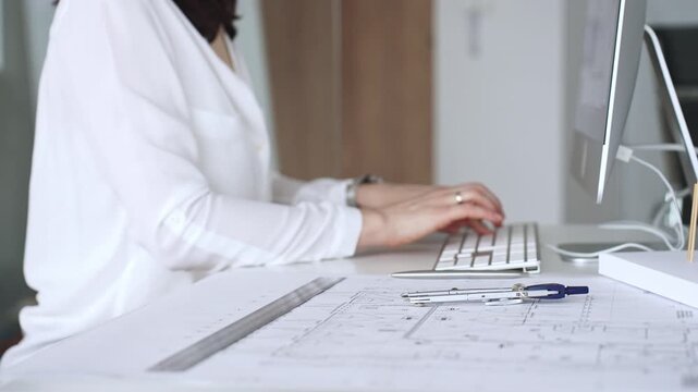 Architect creating new designs, working at a computer in office with blueprints and drafting tools. Business and architecture concept