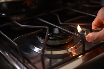 Hand lighting gas stove burner with butane lighter in kitchen, close-up indoor cooking ignition