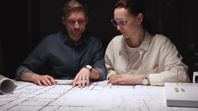Architects and engineers collaborating on a new building project, planning structural details and design concepts using blueprints and a scaled architectural model on a desktop