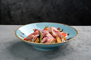 Warm beef salad featuring tender medium-rare slices, crispy potatoes, mixed lettuce, mustard seeds and balsamic reduction on rustic blue plate. Sophisticated gourmet main course