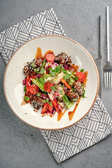 Warm beef salad featuring sesame-crusted teriyaki meat pieces, crisp lettuce, radicchio, microgreens and tangy sauce drizzle on white ceramic plate. Flavorful Asian fusion appetizer