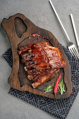 Sticky BBQ pork ribs glazed with sweet and spicy sauce on wooden serving board. Tender grilled spare ribs with rosemary and chili pepper garnish, delicious comfort food meal, top view