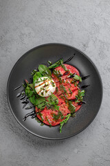 Fresh tomato carpaccio with creamy burrata, pesto drizzle, fresh basil leaves and balsamic glaze on black plate. Elegant Italian appetizer, gourmet salad-style dish, restaurant presentatio, top view