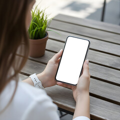 Person holding smartphone with blank screen at outdoor wooden table with plant