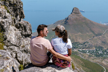 A couple relaxes on the rocky summit of Table Mountain, gazing at the stunning scenery of Cape Town...