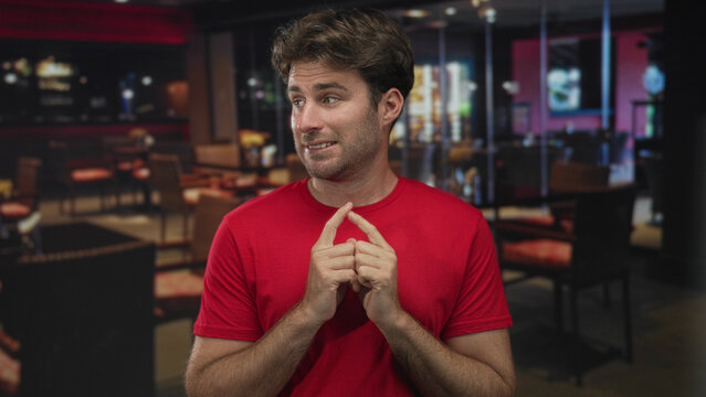 Man with fingertips touching and awkward smile in building restaurant interior; nervousness hesitation uncertainty.