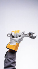 Hand wearing gray and yellow gloves holds an adjustable wrench against a plain white background, showcasing the tool's details and grip strength