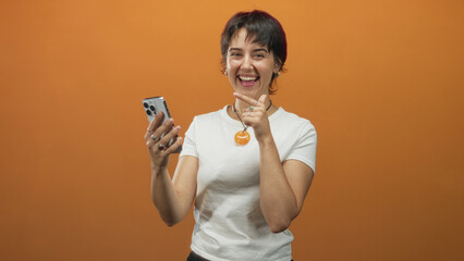 Woman points finger to smartphone in studio, smiling and tapping screen while holding phone with...