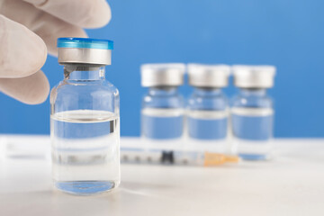 Doctor hand in medical glove holding glass vial of vaccine with blue background, laboratory research and Nipah virus treatment concept