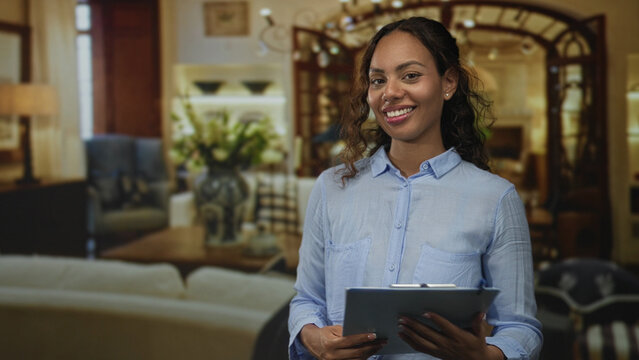 Woman holding clipboard and smiling while reading notes in a living room set inside a building; confidence helpful guidance.